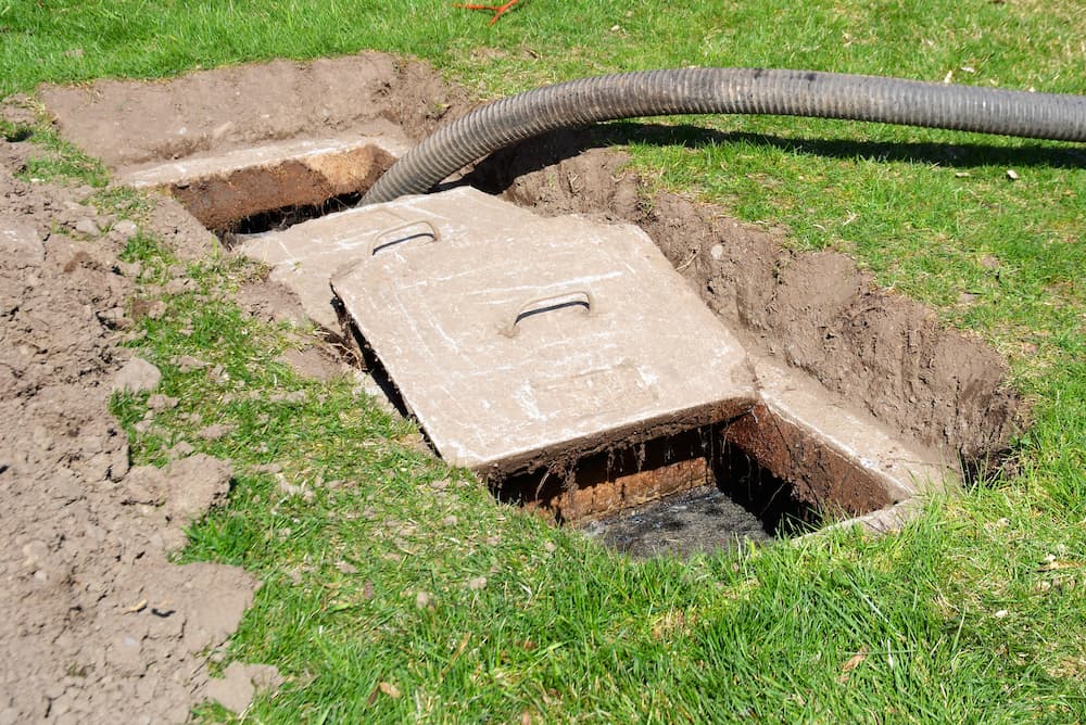 Close-up of a septic tank lid removed with a vacuum hose visible, promoting professional septic tank care and cleaning services.